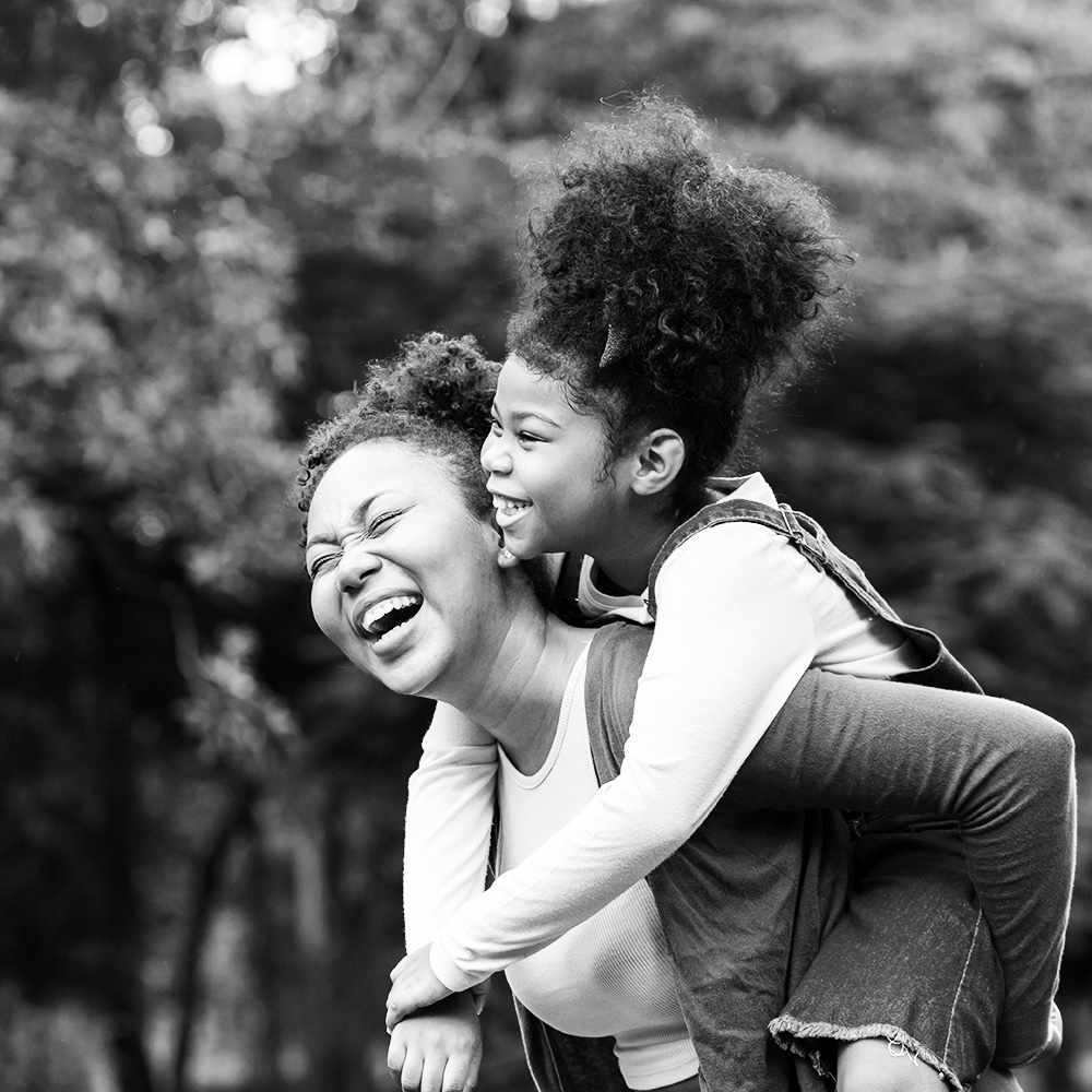 African American mother playing piggyback with daughter in a park