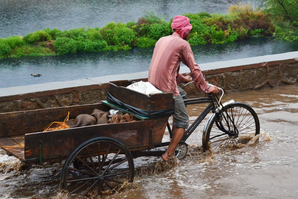 Man hauling material with a bicycle through a flooded street in Asia